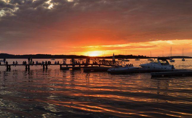 People on a pier below the Memorial Union on Lake Mendota in Madison, WI, watching the sun set on the summer soltice of 2015