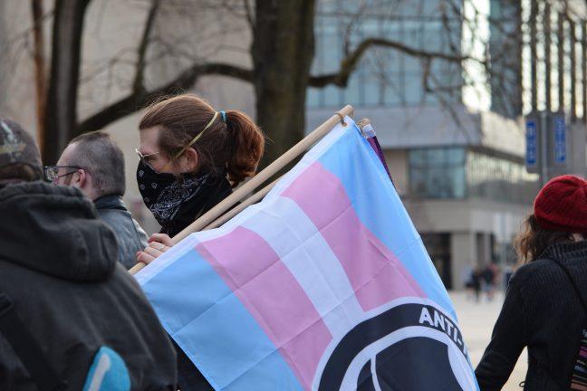 Archival photo of an individual marching with a transgender flag. March 12, 2021.