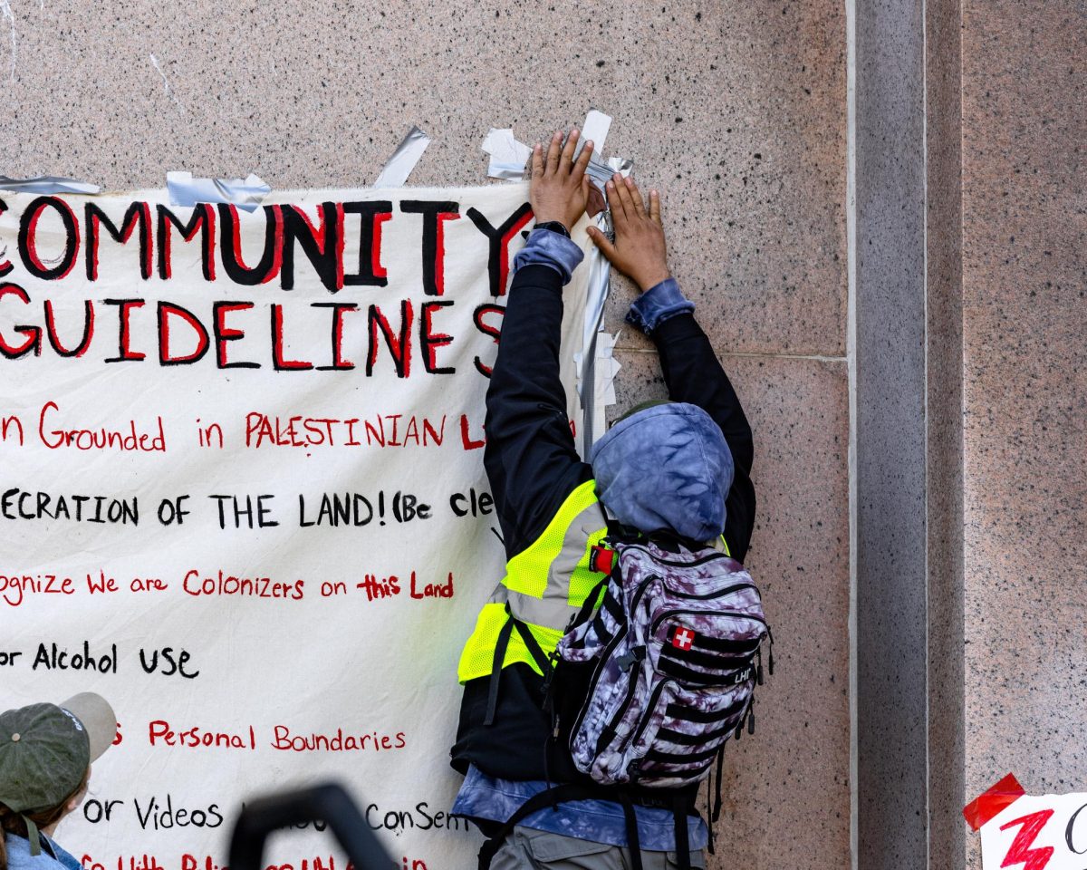 Protest organizer fixes sign hanging on Memorial Library that lists encampment community guidelines. May 3, 2024.