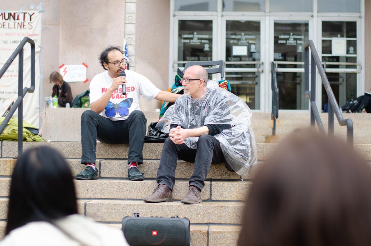 A demonstrator speaks while sitting with Professor Samer Alatout at Library Mall on May 2, 2024.