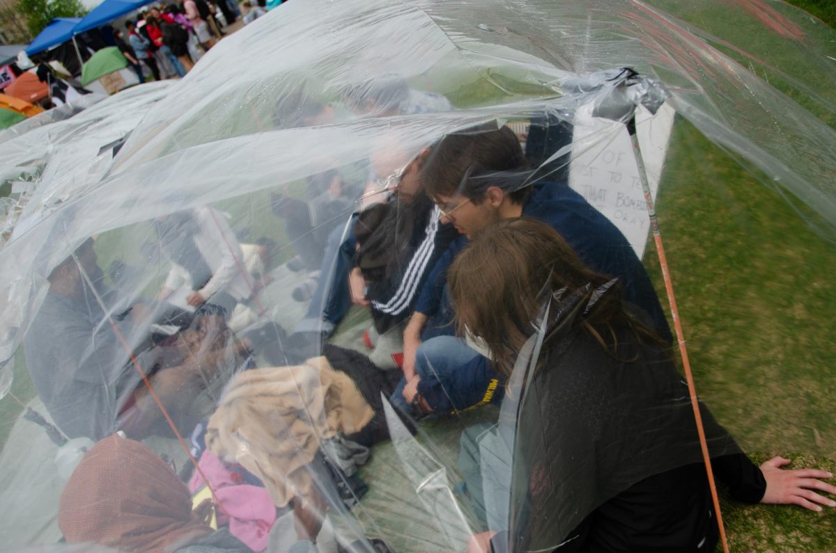 Demonstrators sit together under a plastic covering they pitched to stay dry at Library Mall on May 2, 2024. 