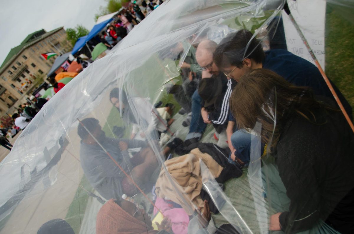 Demonstrators sit together under a plastic covering they pitched to stay dry at Library Mall on May 2, 2024. 