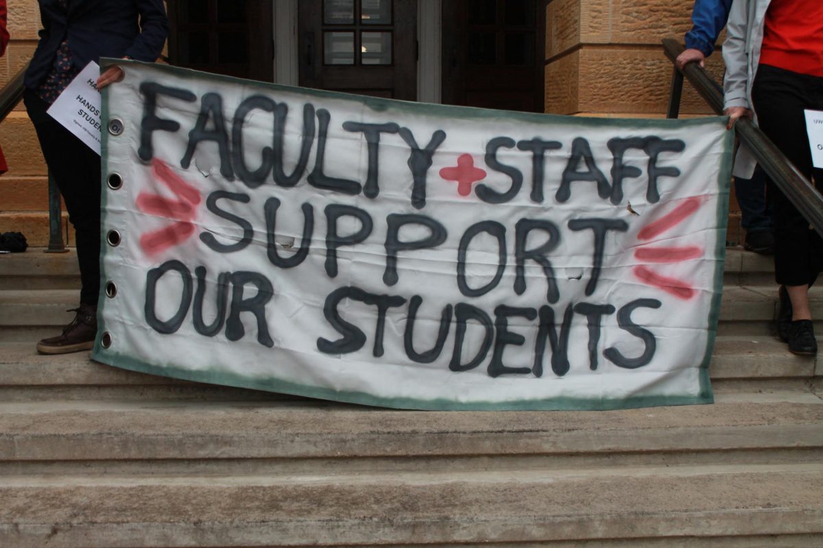 Faculty protest outside of Bascom Hall. Two faculty hold this sign reading FACULTY + STAFF SUPPORT OUR STUDENTS. May 2, 2024.