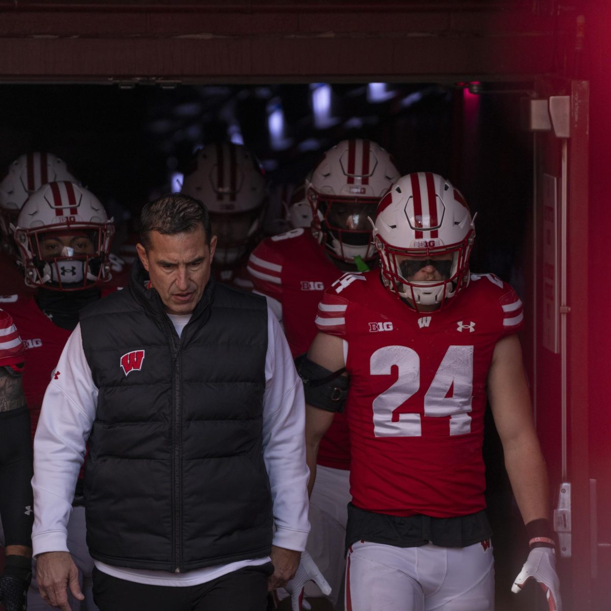 Head coach Luke Fickell walks out of the tunnel onto the field, flanked by players. November 29, 2024. 